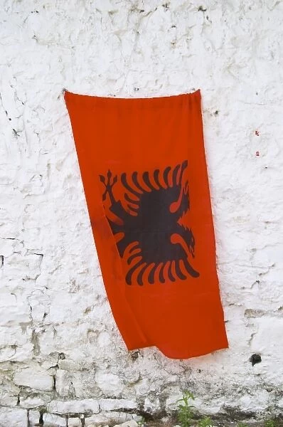 The Albanian flag, red with black double headed eagle, against a white washed stone wall
