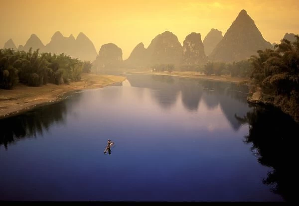Asia, China, Guangxi Province, Yangshuo. Lone fisherman works calm waters of the Li River