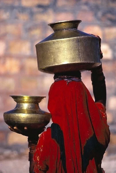 Asia, India, Rajasthan. A local woman in a red sari skillfully balances brass water