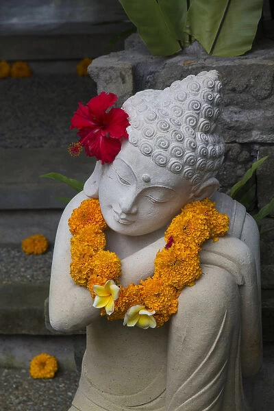 Asia, Indonesia, Bali. Sacred statue with red Hybiscus flower and yellow Marigold necklace