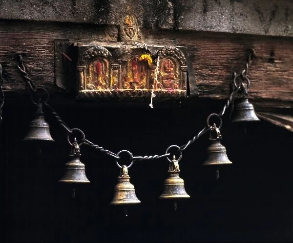 Asia, Nepal, Kathmandu Valley. Brass bells hang from a chain below an offering site
