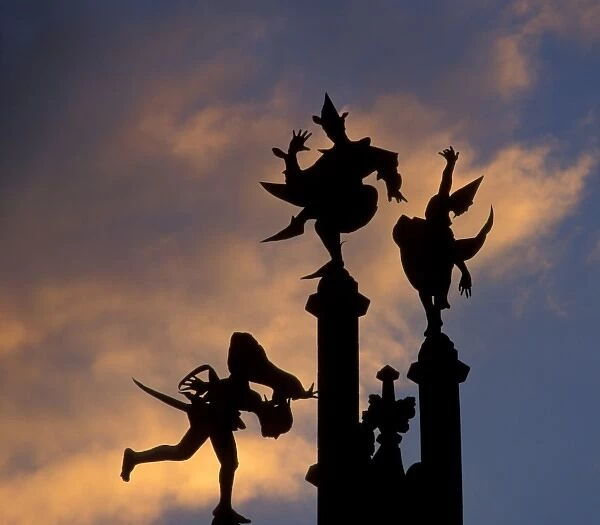Belgium, Ghent. Silhouette of stone figures atop building, colored cloud background