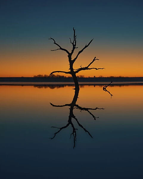 Calm day at a Kansas lake creating reflections of the illuminating blue and orange sky