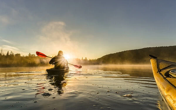 Canada, British Columbia. A kayaker paddles in sunlit early morning mist on a Canadian