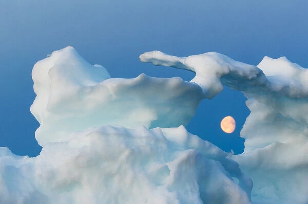 Canada, Nunavut, Territory, Moonrise framed in arch of melting iceberg along Frozen