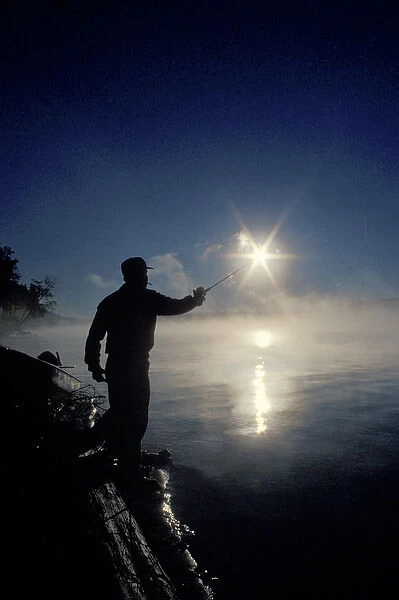 Canada, Ontario, Silhouette of fisherman casting a line into lake on a summer sunrise
