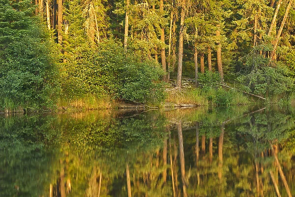 Canada, Ontario. Sunset on forest reflected in lake. Credit as