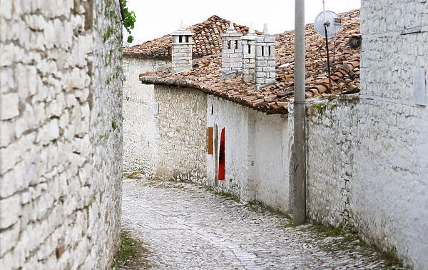 Cobble stone street with traditional ottoman white stone houses. An Albanian flag on the wall