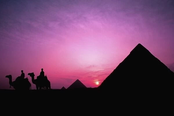Colorful sunset with men with camels silhouetted against the famous Great Pyramids