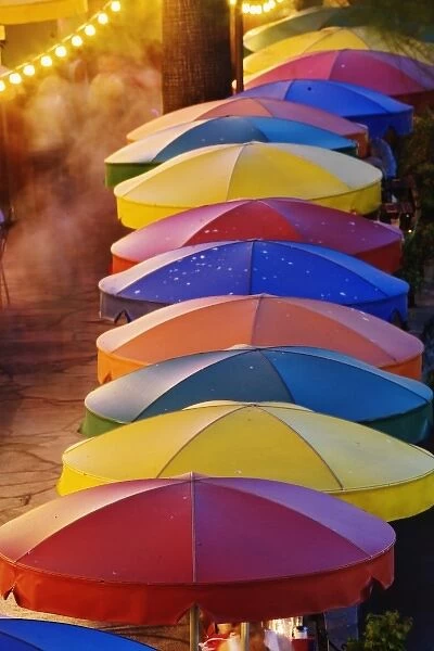 Colorful umbrellas of outdoor cafe and blurred people in motion along famous River Walk