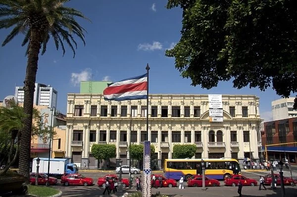 Costa Rican flag, red taxicabs, and yellow buses at the Parque Central in the city of San Jose
