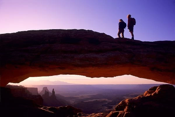A couple watches sunrise from atop Mesa Arch in the Island-in-the-Sky region of Canyonlands