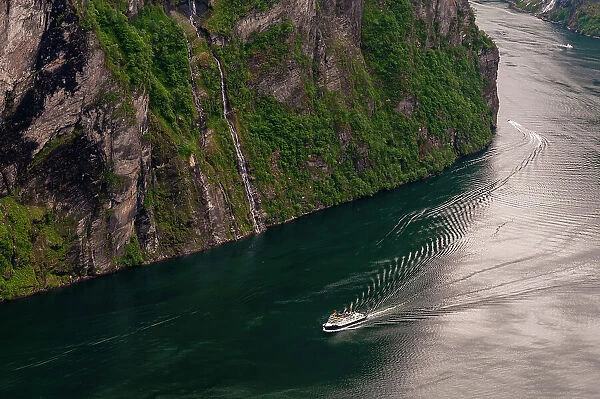 A cruise ship navigates past sheer cliffs in Geirangerfjord, Norway