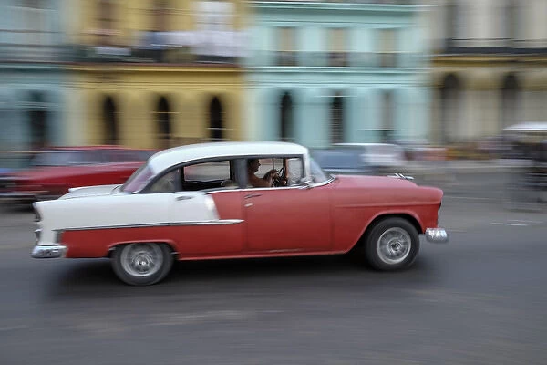 Cuba, Havana. A classic american car zooms along a city street
