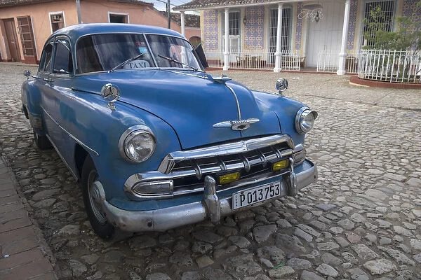 Cuba, Trinidad. Blue taxi parked on cobblestones