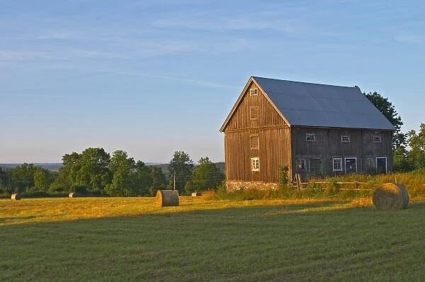 Cut field with hay bales at sunrise. Old farm house barn. Traditional style Swedish