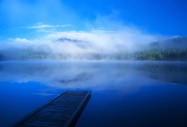 An empty dock on a calm misty lake