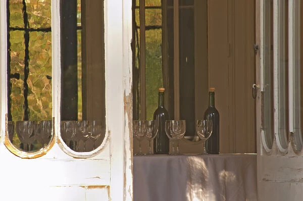 Door open to the garden with inside a table set with glasses and bottles for tasting wine