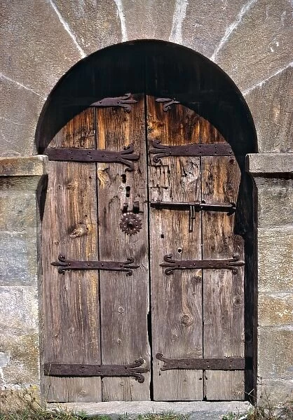 Europe, Andorra. An ancient old wooden door contrasts against a stone building in Andorra