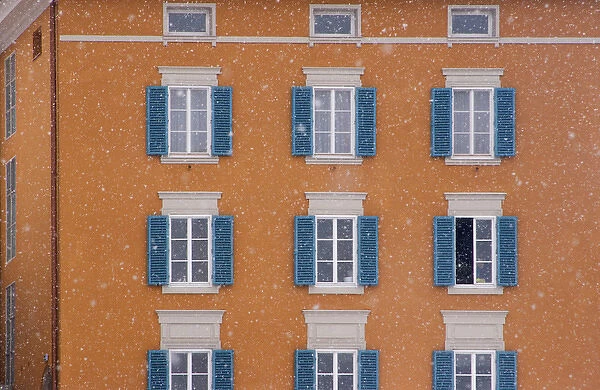 Europe, Austria, Salzburg. Blue shutters on orange apartment building in snowfall