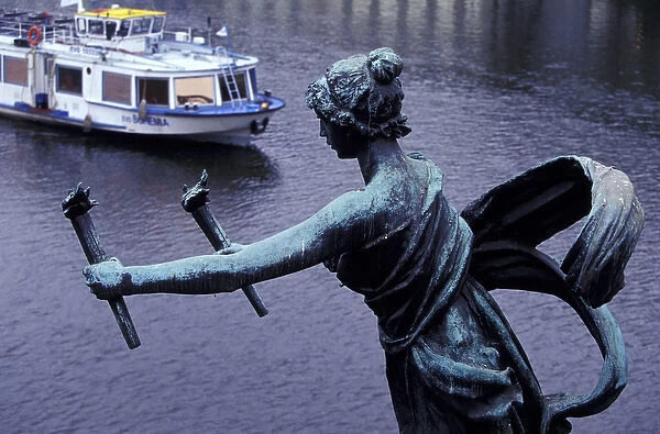 Europe, Czech Republic, Prague. Statue on Cechuv Bridge with cruise boat in background