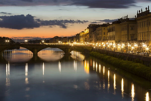 Europe, Italy, Florence. As dusk falls, city streetlights illuminate the riverfront streets