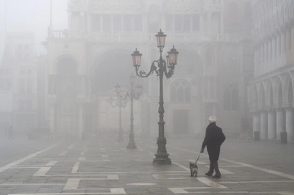 Europe, Italy, Venice. A man walks his dog in San Marco Square near the Doge s