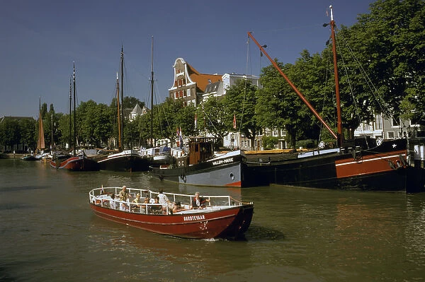 Europe, Netherlands, Dordrecht. Boats lining canal, with tourist boat motoring by