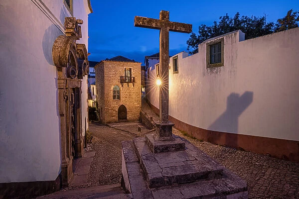 Europe, Portugal, Obidos. Church and cross on cobblestone street at sunset