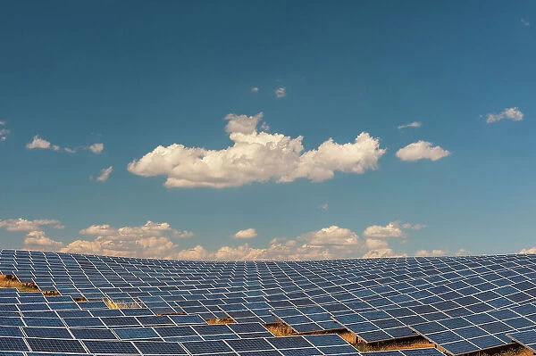 A field of solar panels at a solar power plant under a blue sky with puffy white clouds. Les Mees, Provence, France