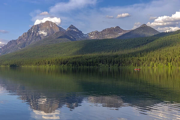 Fishing from a red canoe on the calm waters of Bowman Lake in Glacier National Park