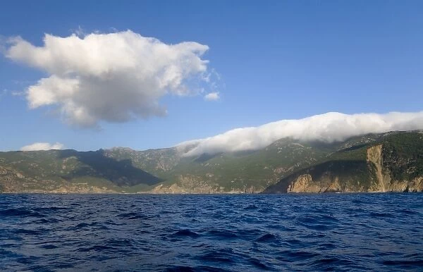 France, Corsica. Clouds blow over peaks in high wind. View from off the coast near Galeria