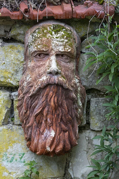 France, Giverny. Stone face hanging on a stone wall. Credit as