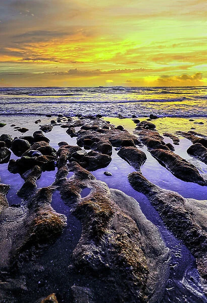 The golden light of the setting sun reflects a gold glow on the beach at Pererenan Beach, as the waves roll in on Bali, Indonesia