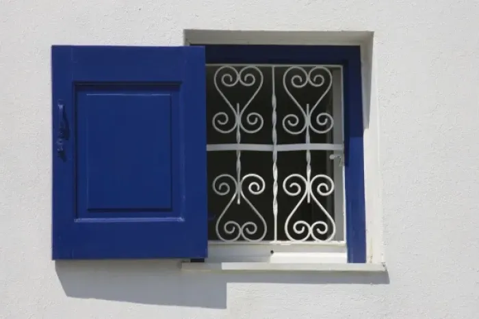 Framed Print : Greece, Mykonos, Hora. Open window with blue shutter and iron grill contrast with white wall