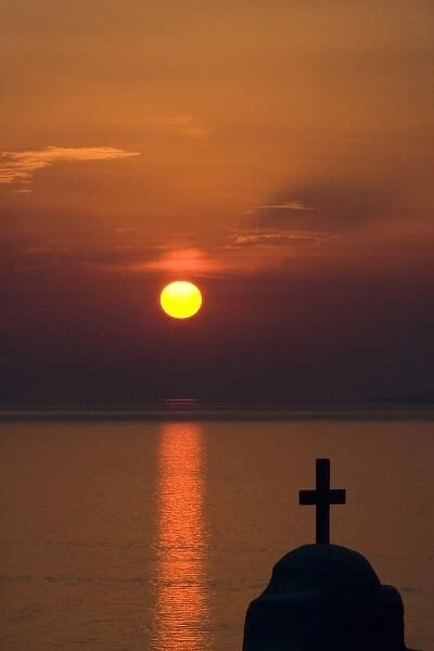 Greece, Mykonos, Hora. Sunset silhouettes Greek Orthodox church and cross in foreground