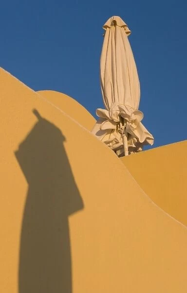 Greece, Santorini. Folded sun umbrella and shadow of another umbrella against yellow wall