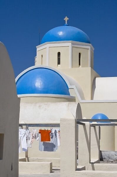Greece, Santorini, Thira, Oia. Blue Greek Orthodox church domes contrast with drying laundry
