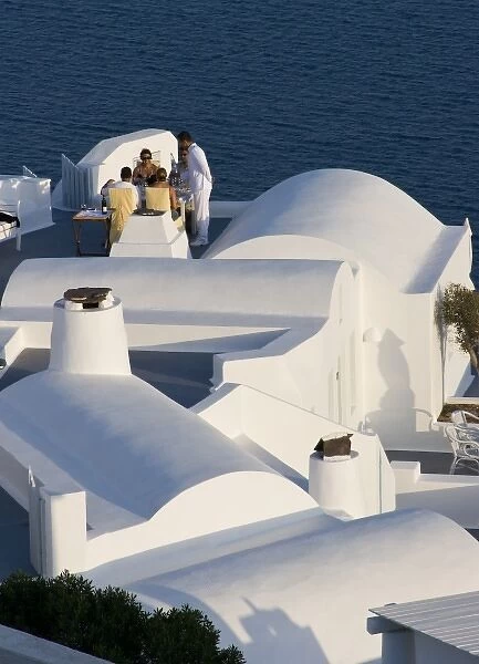 Greece, Santorini, Thira, Oia. Two couples are served for dinner at white villa overlooking sea