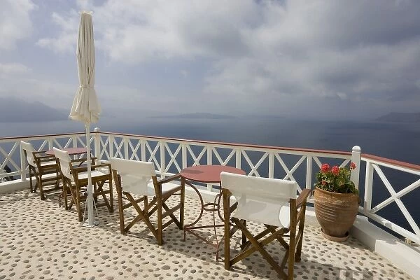 Greece, Santorini, Thira, Oia. Patio tables and chairs on pebbled deck overlooking misty sea