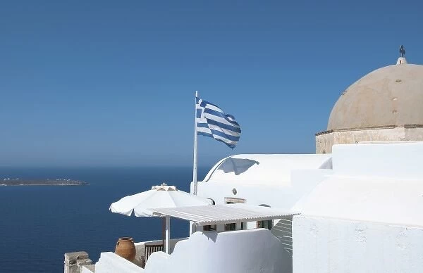 Greek flag flying on porch of white home on steep clifees of Fira in Santorini in