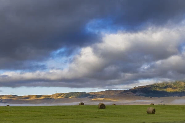 Hay bales in clearing fog with Salish Mountains in Lake County, Montana, USA