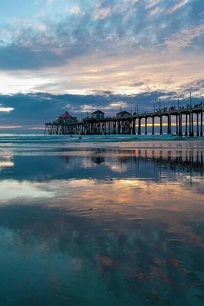 The Huntington Beach Pier and reflections on the wet beach at sunset. Huntington Beach, California
