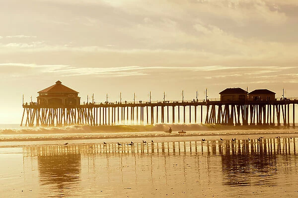 The Huntington Beach Pier and surfers at sunset. Huntington Beach, California