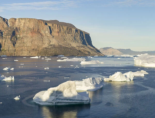 Iceberg in the Uummannaq Fjord System. Red cliffs of Storoen Island in the background