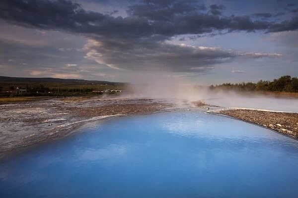 Iceland, Geysir, Rising sun lights deep blue thermal pool and steam venting