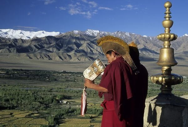 India, Ladakh, Thikse. Buddhist monk blows conch horn announcing prayers from rooftop