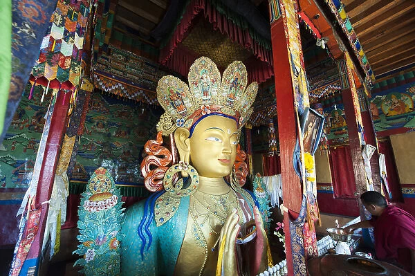 India, Ladakh, Thiksey, monk making offerings to golden Maitreya Buddha inside Thiksey Monastery