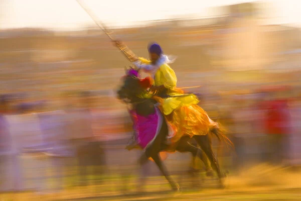 India, Punjab, Anandpursahib. Blurred rider and horse ride past crowd at Hollamohalla Festival
