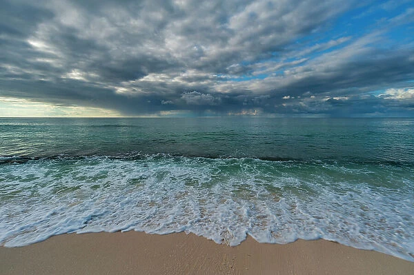 Indian ocean surf surging onto a sandy beach, under a dramatic cloud-filled sky. Denis Island, Seychelles